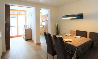 A modernly furnished dining area with a table and chairs. The open kitchen is visible in the background and creates a bright, inviting atmosphere.