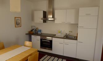 A modern kitchen with white cabinets and a stove. A dining table with wooden chairs is nearby.
