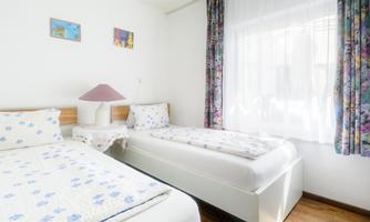 A bright bedroom with two single beds and colorful curtains. The room has a large window that lets in natural light.
