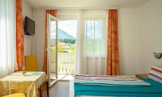 A bright room with colorful curtains and a bed in blue and striped colors. From the balcony, there is a beautiful view of the surrounding landscape.