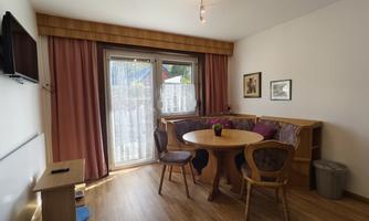 A cozy interior with a round table and chairs. Large windows provide daylight and a view outside.