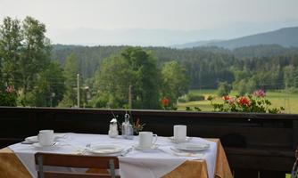 A set table on a terrace overlooking green meadows and mountains. The surroundings are calm and inviting.