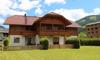 A beautiful house in Alpine style with a balcony and garden. Surrounded by green hills and blue skies.