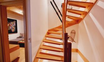 A wooden staircase leads up to a bright hallway. Skis hang on the wall and there is a cozy seating area in the background.