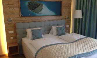 A modern bedroom with a padded bed and wooden walls. The painted wall features a tropical island view.