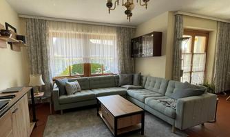 A cozy living room with a gray sofa and a wooden coffee table. Large windows let in plenty of light and offer a view of the outdoors.