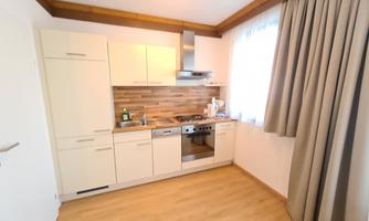 A modern kitchen with light, minimalist furniture and wooden paneling. Plenty of daylight streams in through the window, creating an inviting atmosphere.