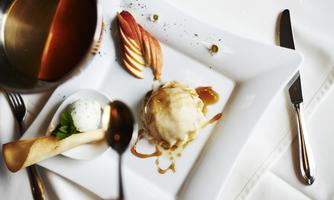An attractively arranged dessert on a white plate. It consists of a scoop of ice cream, caramelized apples, and a crispy pastry roll.