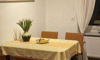 A cozy dining area with a table and four chairs. On the table, there is a bowl of fruit and a vase with fresh flowers.