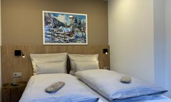 A modern bedroom with two beds and bright bedding. A colorful painting hangs on the wall.