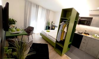 A modern apartment with a corner for the bedroom and a functional kitchen. Green accents and plenty of light create an inviting atmosphere.
