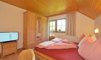 A cozy bedroom with a double bed and wood-paneled walls. The decor is rustic, and there is a television as well as a large wardrobe.