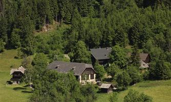 A quiet, green landscape with several traditional buildings. Surrounded by dense forest and meadows.
