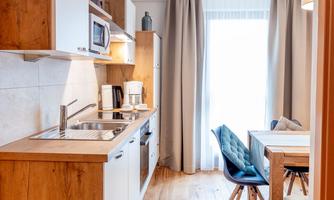 A modern kitchen with wooden cabinets and a dining area. Plenty of daylight streams through the window.