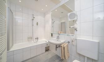 A modern bathroom with a bathtub, a sink, and a large mirror. The walls are brightly tiled and well lit.