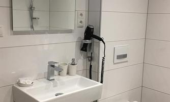 A modern bathroom with a sink, mirror, and shower. The walls are designed in white tiles.