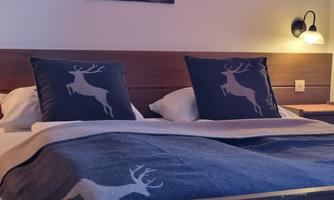 A cozy bedroom with a double bed and cushions featuring a deer motif. There is soft lighting and a calm atmosphere.