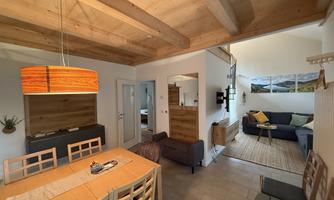 A cozy living area with wooden ceilings and modern furniture. The room is bright and welcoming, with a dining area and a living room.