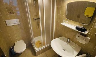 A small, clean bathroom with a shower, sink, and toilet. The walls are brightly tiled and there are some towels and toiletries.