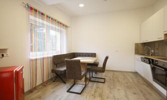A modern kitchen with a dining area and a large window. The room is bright and friendly with a red refrigerator and stylish furniture.