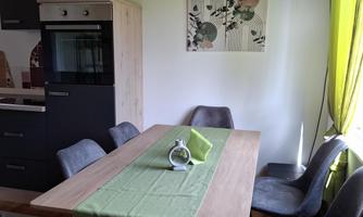 A modern kitchen with a dining table and chairs. Green tablecloths and natural wood details create an inviting atmosphere.