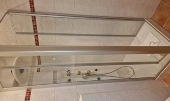 A modern shower enclosure with glass walls and a rain shower head. The space is brightly tiled and appears clean and inviting.