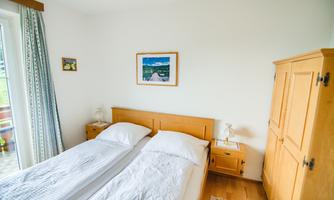 A cozy bedroom with two separate beds. The walls are light, and a simple wooden shelf complements the decor.