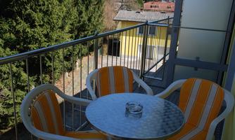 A cozy balcony with two orange-striped chairs and a small table. In the background, there are trees and a yellow building.