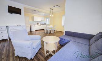 A bright living room with modern design and a cozy sofa. The room features a dining table and a fully equipped kitchen.