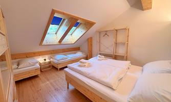 A cozy bedroom with wooden beds and a large window. There are two single beds and a wardrobe.