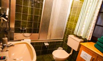 A small bathroom with a shower, bathtub, and a sink. The walls are decorated with green tiles and there are some towels on a wooden shelf.