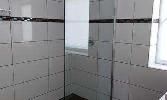 Modern shower in a bathroom with white tiles and a clear glass shower enclosure. Bright room with a window that lets in natural light.