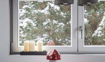 A cozy dining table with a red mushroom figurine, apples, and candles. A snowy landscape can be seen through the window.