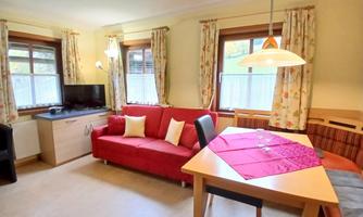 A cozy living room with a red sofa and a dining table. The windows let in plenty of light and the walls are painted in warm colors.