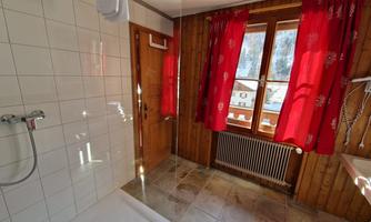 A modern bathroom featuring a shower and a large window front. The red curtains and the wood paneling give the room a cozy atmosphere.
