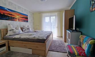 A cozy bedroom with a large double bed and colorful decor. The room features a window with access to the balcony and a television.