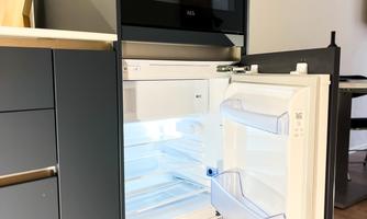 A modern refrigerator with an open door and an empty interior. It is situated in a modern kitchen with a wooden floor.