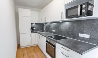 A modern kitchen with white cabinets and a dark countertop. It is equipped with a stove, an oven, and a microwave.