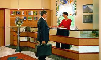 A reception area with a receptionist and a businessman. The man is wearing a suit and holding a briefcase.