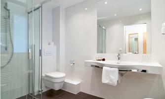 A modern bathroom with a glass shower and a large mirror. It is designed in light colors and feels clean and inviting.