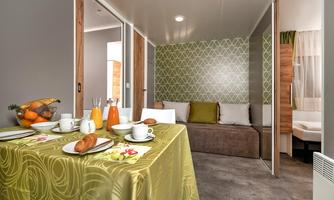 A cozy living space with a set table featuring fresh fruit, beverages, and baked goods. The walls are designed in a modern and friendly manner.
