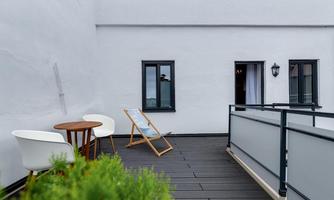 A modern terrace with a wooden floor and a cozy seating area. In the background, two windows and a plant are visible.