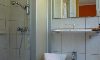 A modern bathroom with a shower and a large mirror. The walls are tiled, and there is a shelf with skincare products.