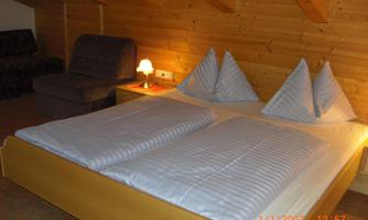 A cozy bedroom with a double bed and two decorative pillows. The wood paneling and soft light create an inviting atmosphere.