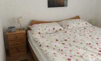 A cozy bedroom with a double bed and colorful bedspreads. A modern painting hangs on the wall, and there is a nightstand with a lamp.