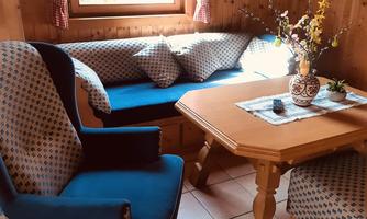 A cozy living space with blue upholstered furniture and a wooden table. The window lets in plenty of daylight and there is a lovely flower decoration.