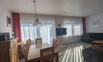 A bright and welcoming apartment with a dining area and a couch. Large windows provide plenty of daylight and a cozy atmosphere.