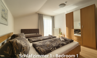 A bright bedroom with two beds and a cozy seating area. Large windows provide plenty of daylight.
