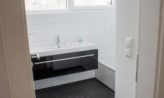 A modern bathroom with a black vanity and a bathtub. Large windows provide plenty of light.