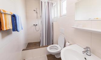 A modern bathroom with a shower, a sink, and a toilet. Colored towels are hanging on a towel rack.
